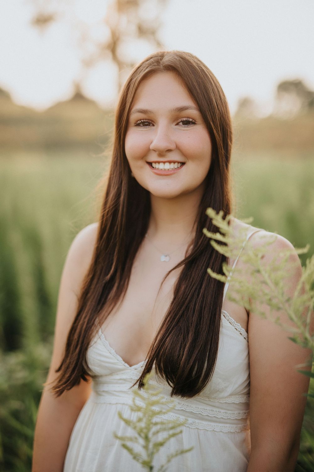 Summer portrait captured in dreamy golden light with white dress and natural foliage backdrop.