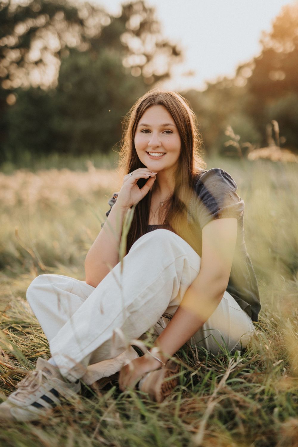 A person in white clothing reclines in a field of tall grass during sunset.
