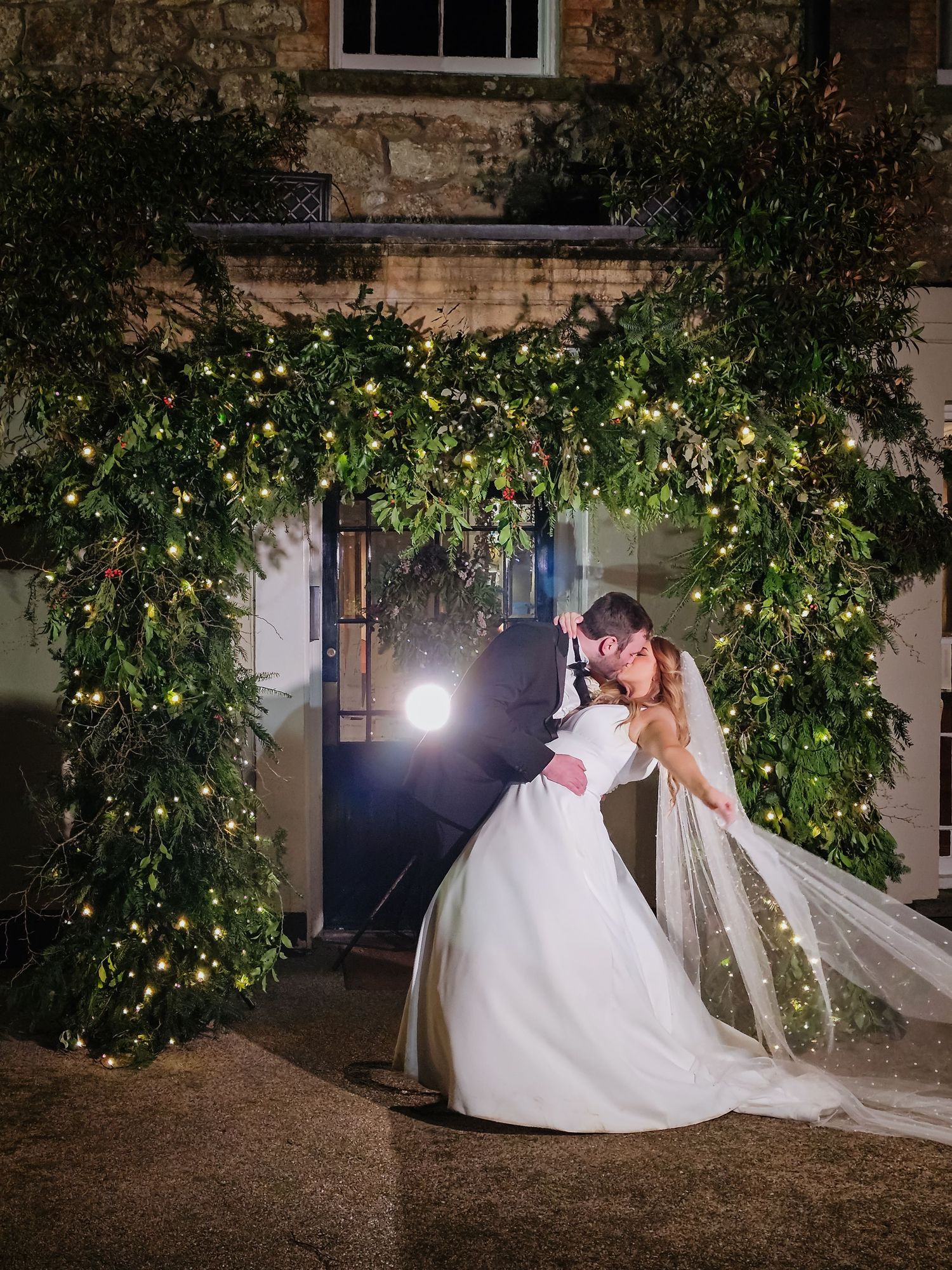 A romantic evening wedding photo series under twinkling lights and foliage at a rustic venue.