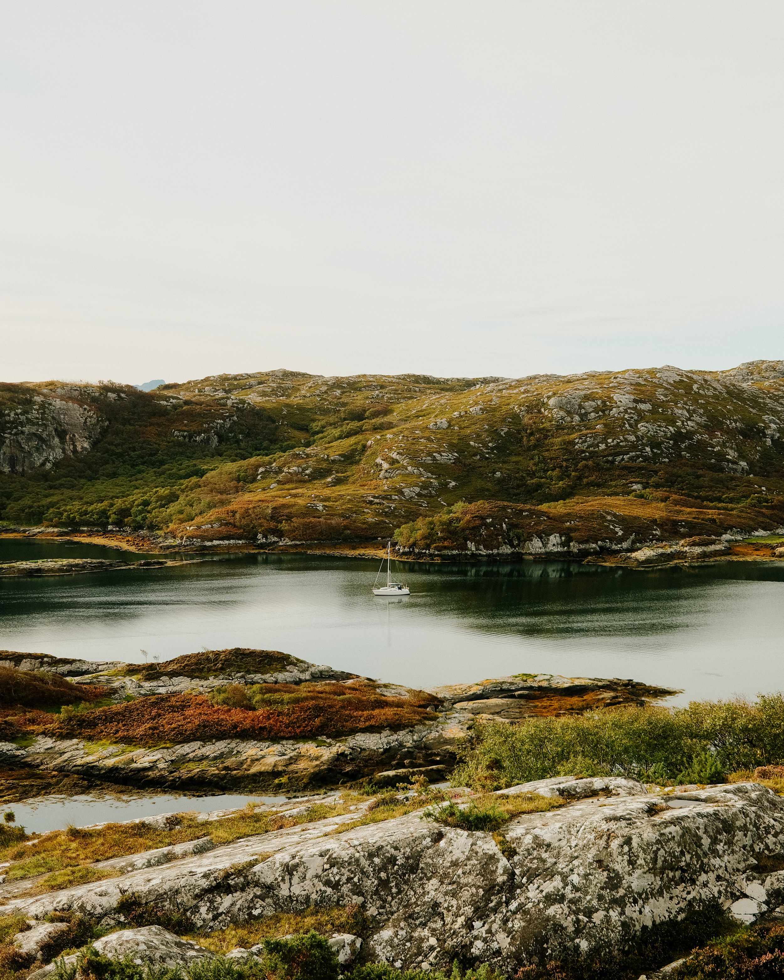 Rocky coastal landscape with calm bay waters and rugged terrain under overcast sky.
