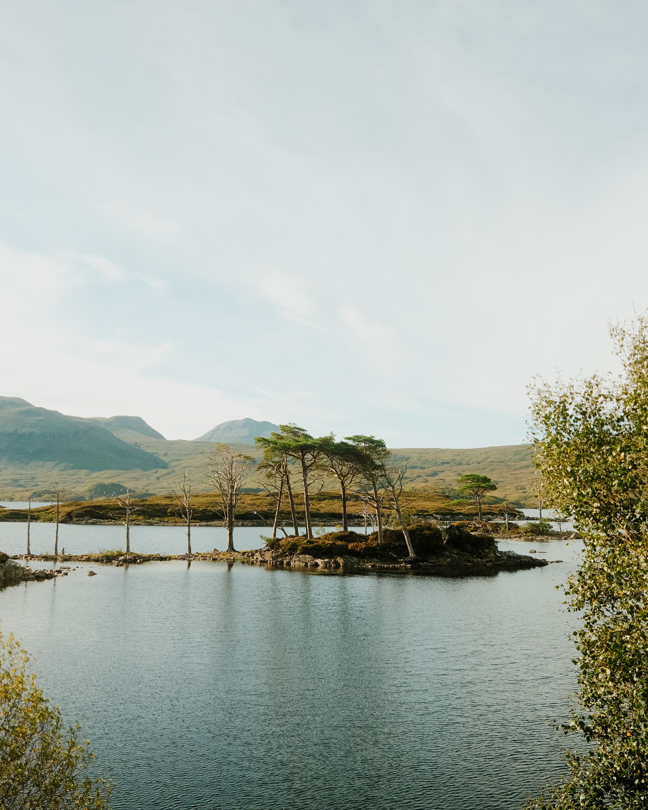 Panoramic view of a serene lake with small islands and mountains in the background on a cloudy day.
