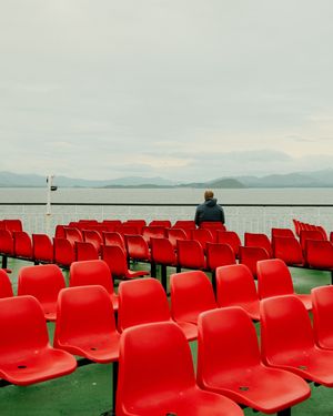 Rows of bright red stadium seats overlook a scenic waterfront view with mountains in the distant horizon.