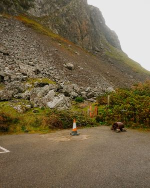 A panoramic view of a rocky mountain slope with a gravel parking area at the base in foggy weather.