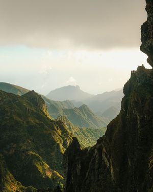 Dramatic mountain landscape with jagged peaks and deep valleys bathed in golden sunlight against a misty sky.