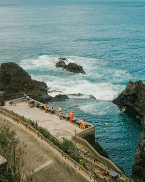 Aerial view of a winding coastal path with scenic overlooks along rugged cliffs and crashing waves against rocky shores.