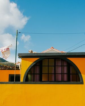 A bright yellow wall with curved architectural arches and windows against a vibrant blue sky.