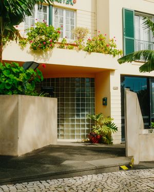 Yellow stucco building with green shutters and glass block windows along a cobblestone driveway.
