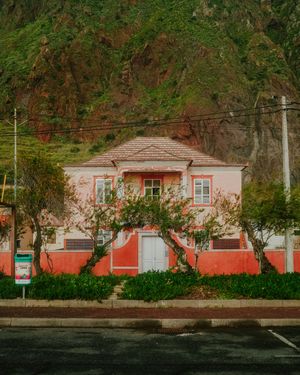 Charming pink and coral house with white trim and trees sits against a lush green mountainside backdrop.