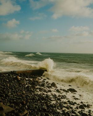 Dramatic waves crash against a rocky shoreline under cloudy skies creating a dynamic seascape view.