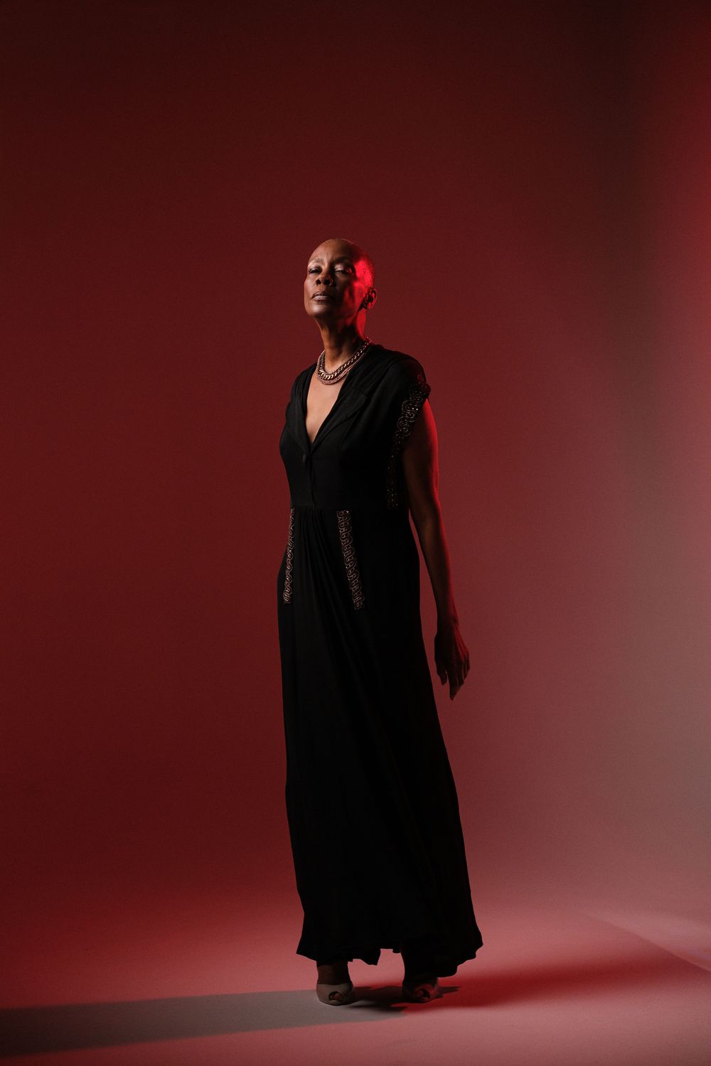 Silhouetted figure in flowing black dress poses dramatically against deep red backdrop.