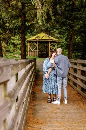 A couple shares a romantic moment on a wooden bridge surrounded by lush forest greenery.