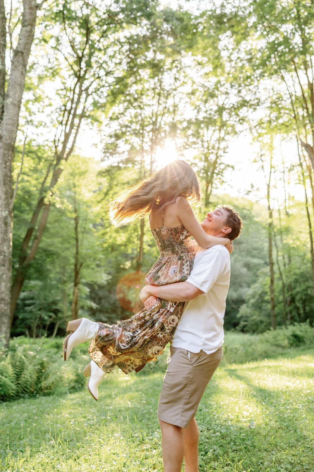 A playful couple twirls and dances in a sunlit forest clearing during golden hour.