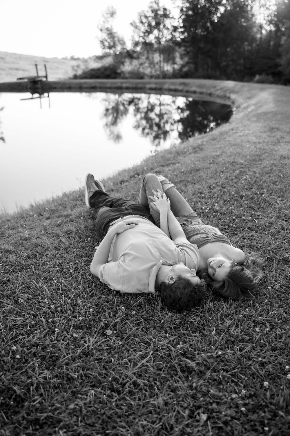 A couple lies peacefully on a grassy hillside in black and white photography.