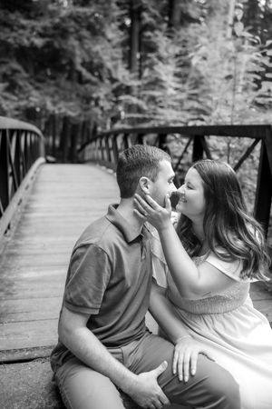 A romantic moment captured in black and white on a wooden bridge surrounded by forest.