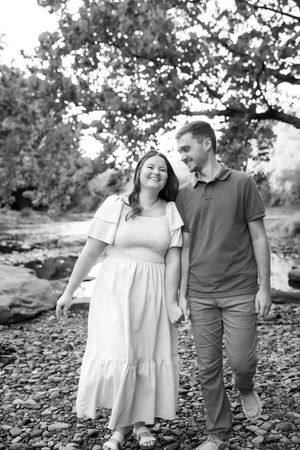 A couple walks hand in hand along a rocky riverbed in black and white photography.