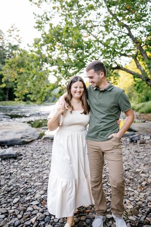 A couple shares joyful moments together on a rocky riverbed during a sunny afternoon.