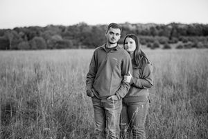 A couple poses together against a backdrop of an open field at dusk.