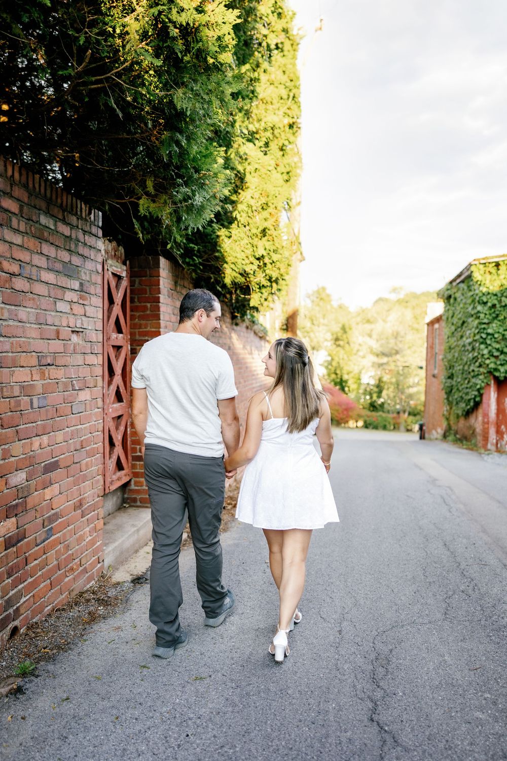 A couple walks hand in hand down a brick-lined path during sunset.
