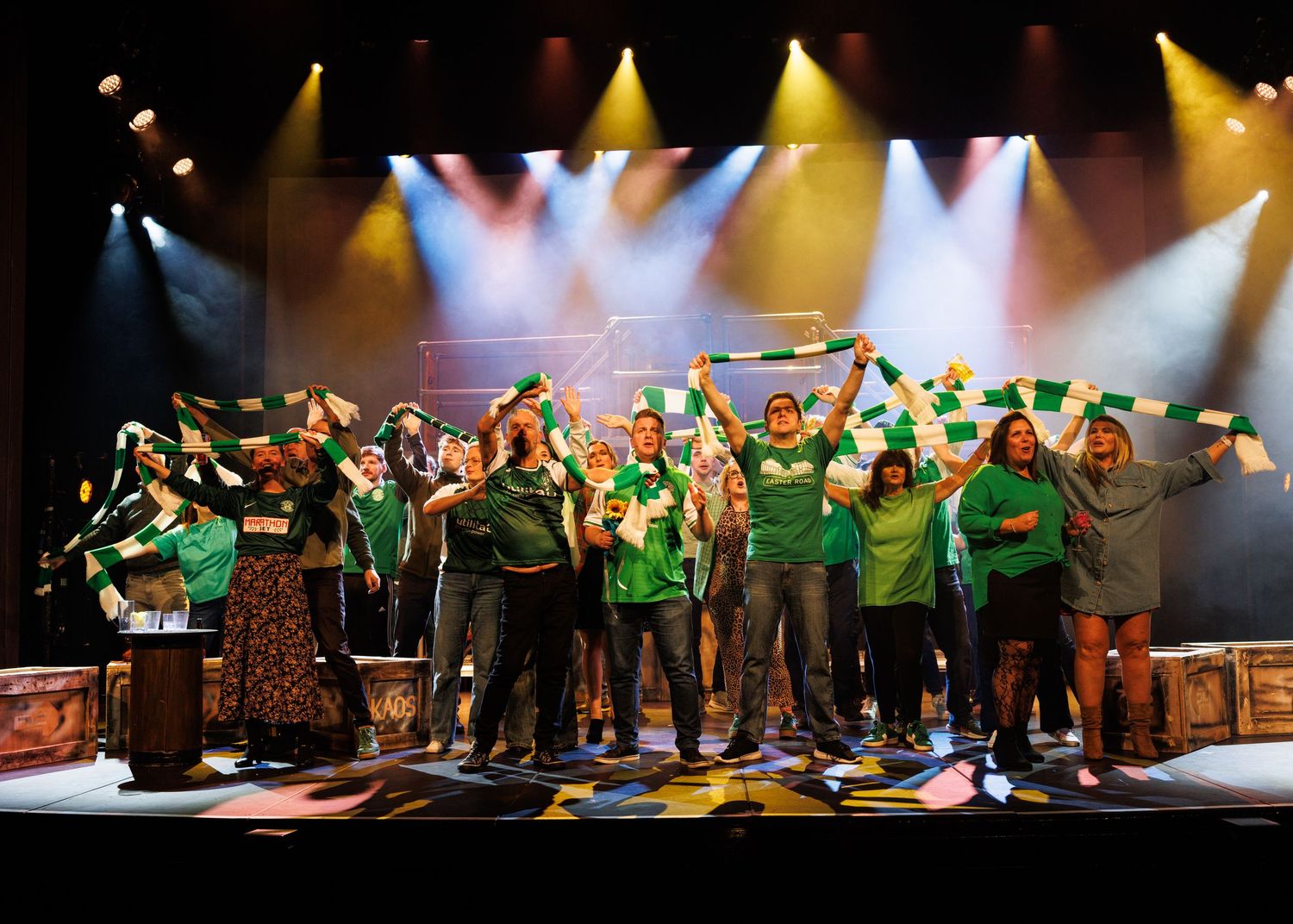 Performers in green shirts dance in formation on a dimly lit stage during a choreographed show.
