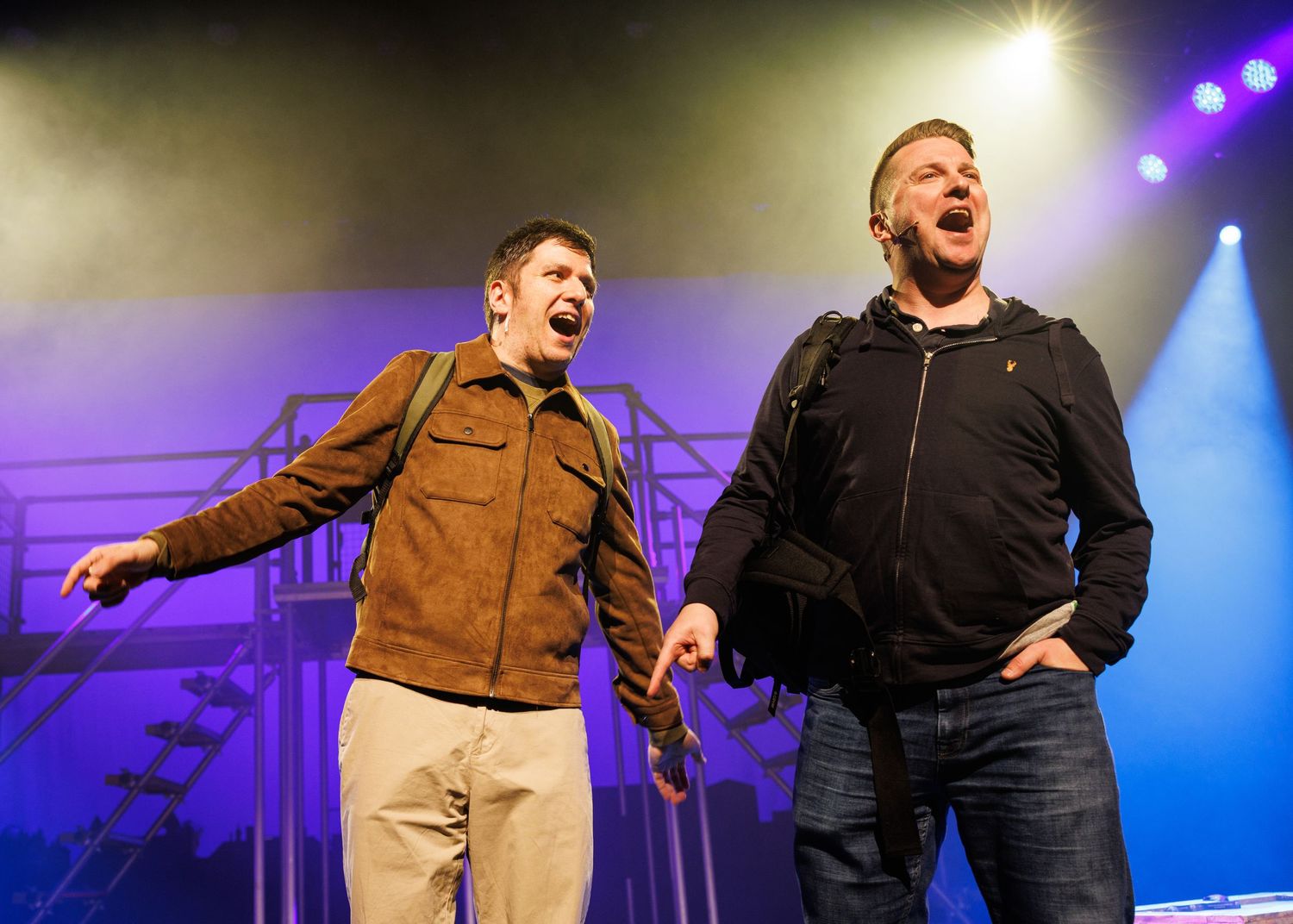 Performers on stage with dramatic blue and purple lighting create dynamic poses during a theatrical production.