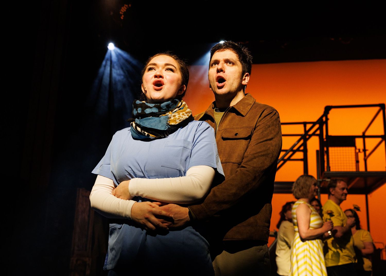 Two performers embrace dramatically on a dimly lit stage during an emotional theatrical scene.