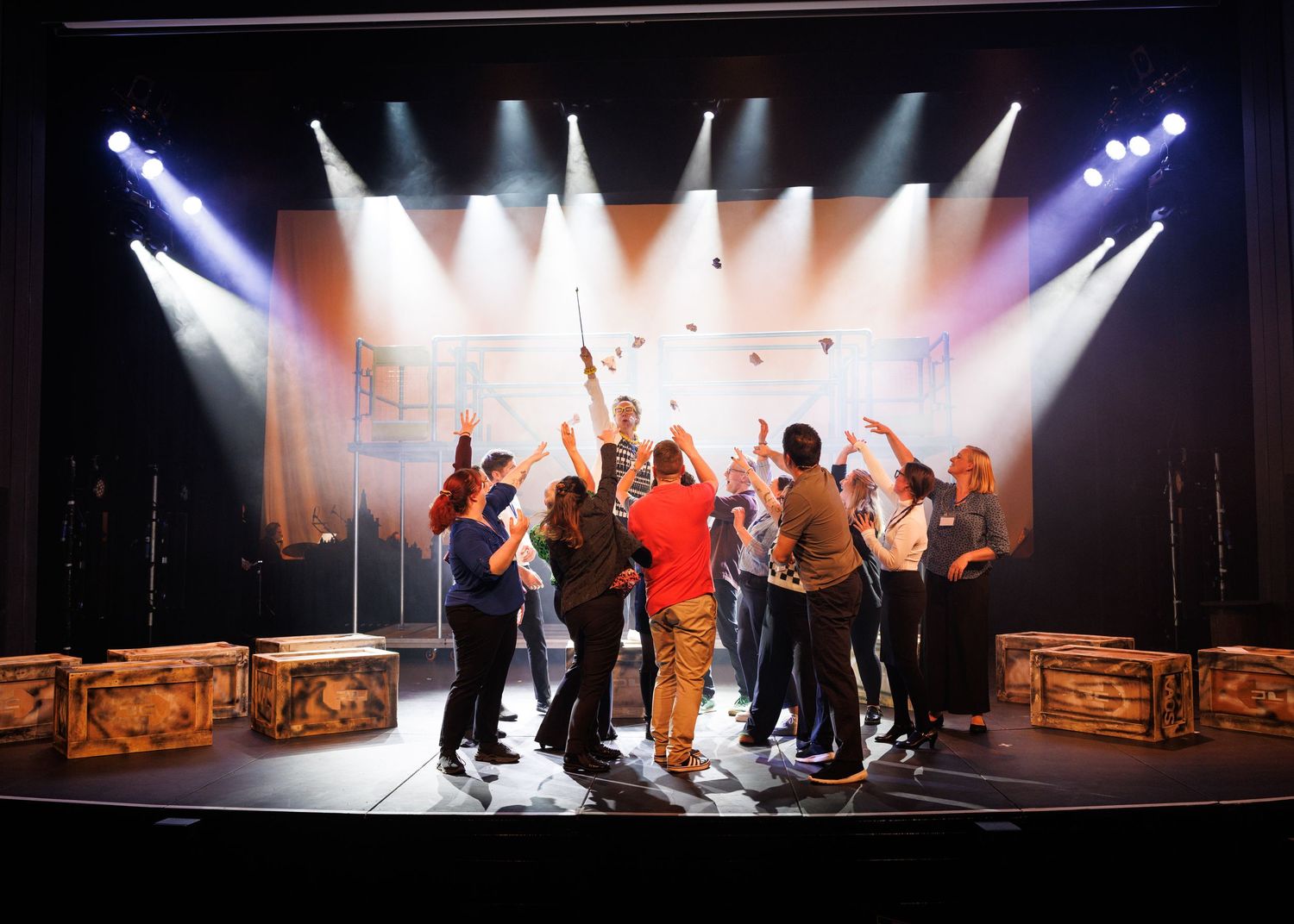Dramatic stage performance with silhouetted figures and bright spotlights creating an atmospheric theatrical scene.