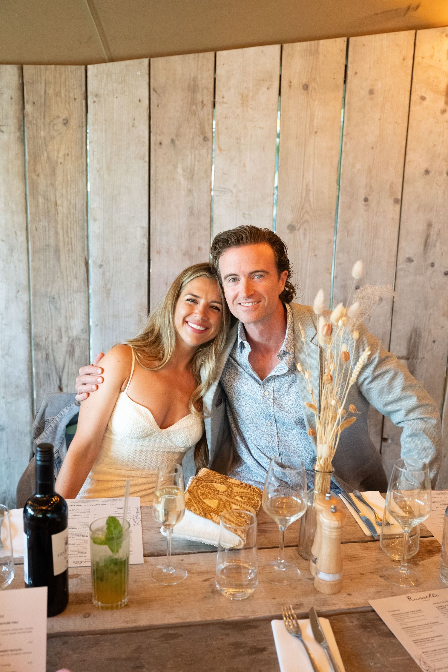 Elopement dinner in Doolin, Ireland with a couple sitting together at a rustic restaurant table with cocktail glasses and dried floral decor