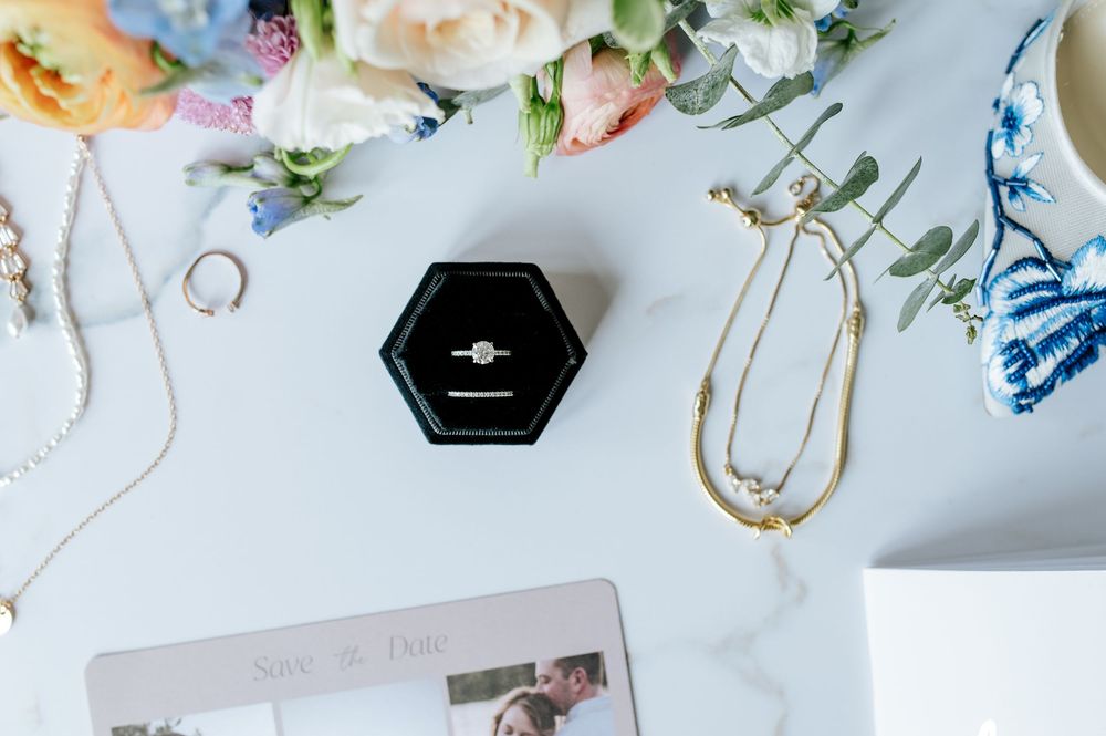 Wedding rings displayed on a white surface surrounded by delicate pink and white roses and floral arrangements.