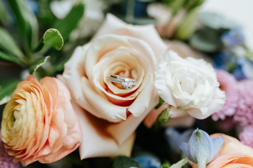 Close-up detail of elegant wedding rings nestled among soft peach and cream colored roses.
