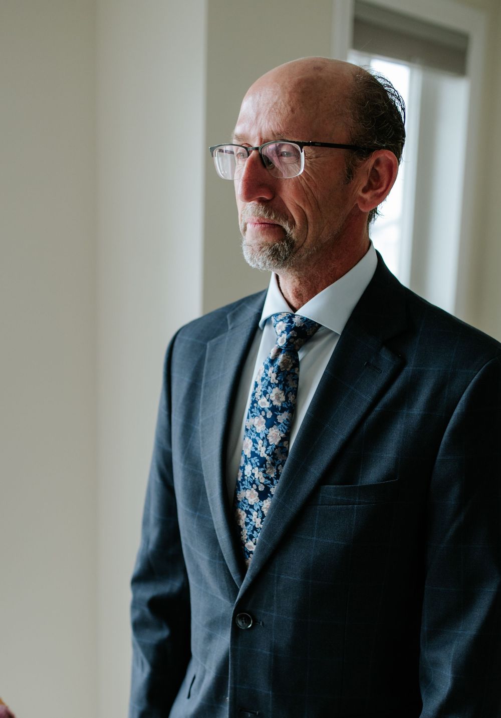 Man wearing glasses and dark suit with floral tie photographed in natural window light.