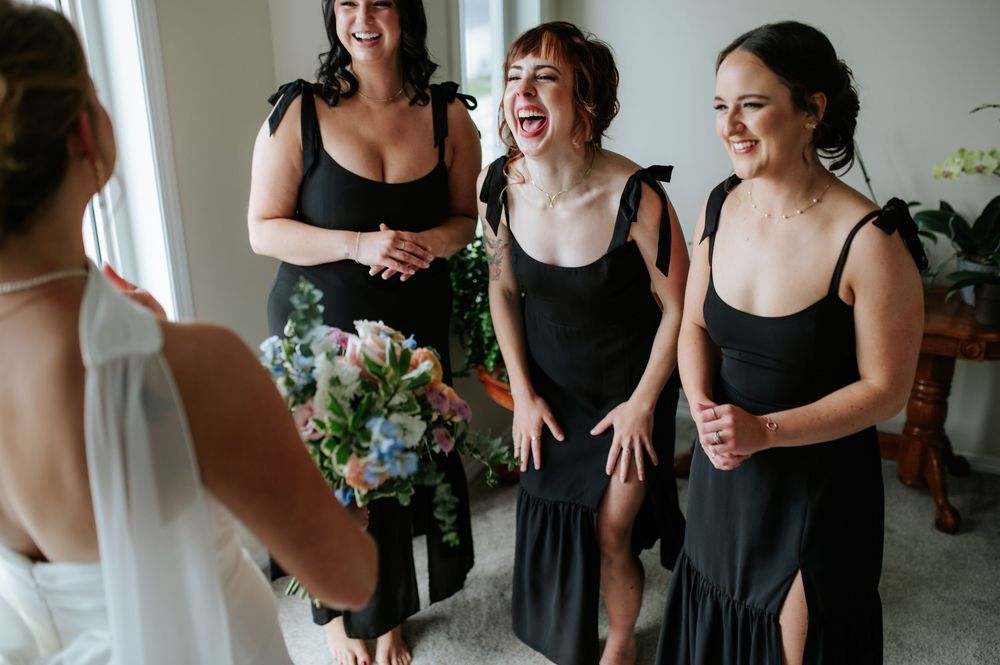 Wedding party in black dresses sharing laughter and candid moments together.