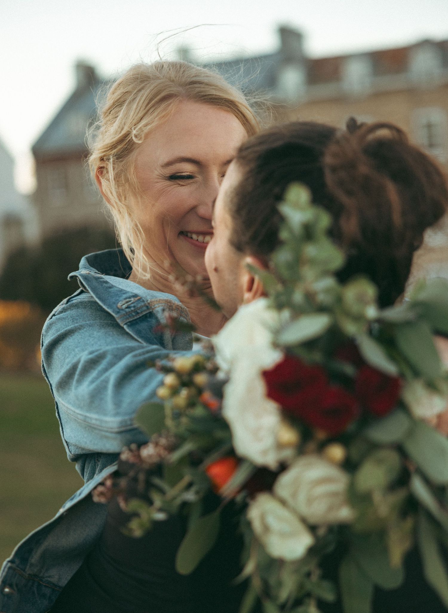 A person in denim holds a vibrant bouquet of white and burgundy flowers against a soft blurred background.