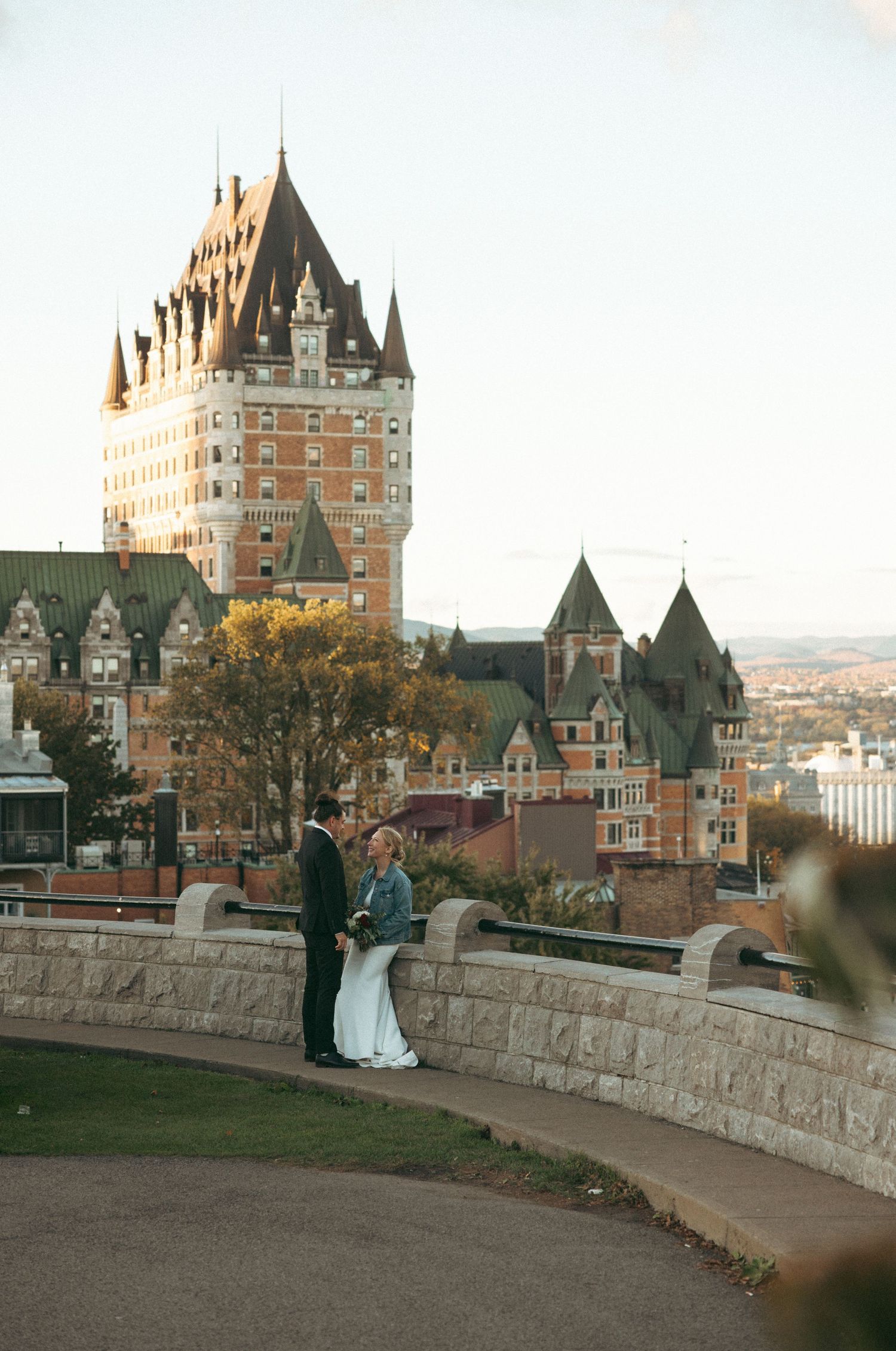 A couple poses in front of the iconic Chateau Frontenac castle hotel in Quebec City at sunset.