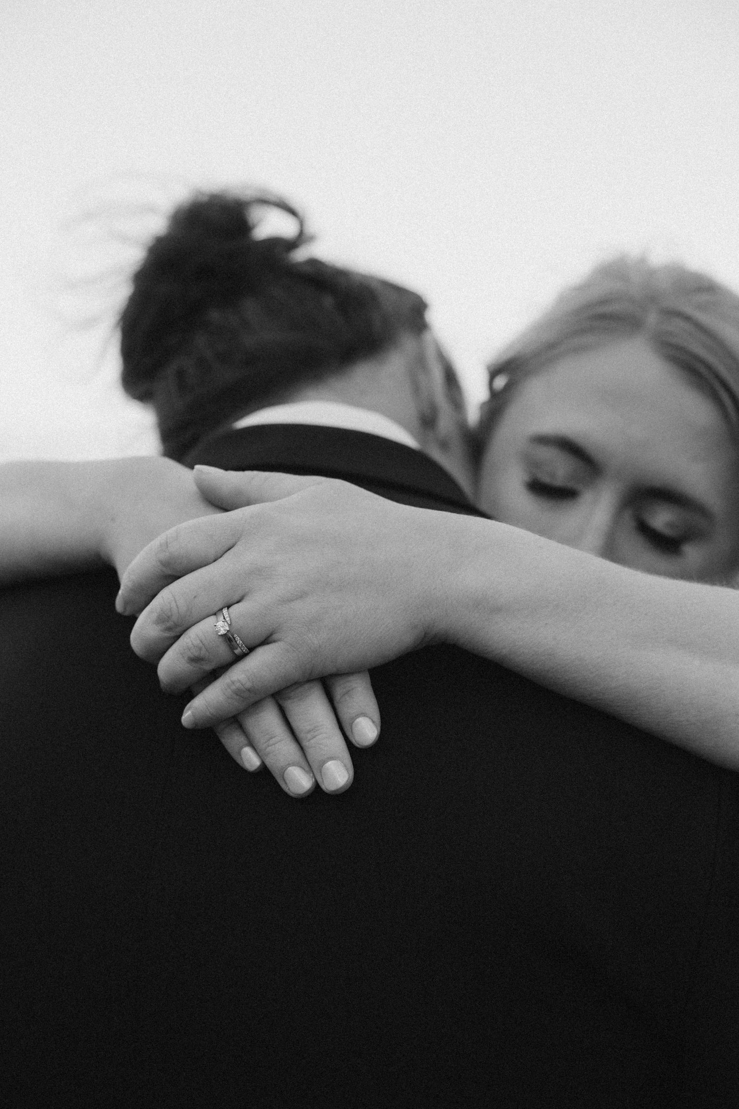 Close-up black and white photo of hands gently resting together showing wedding ring.