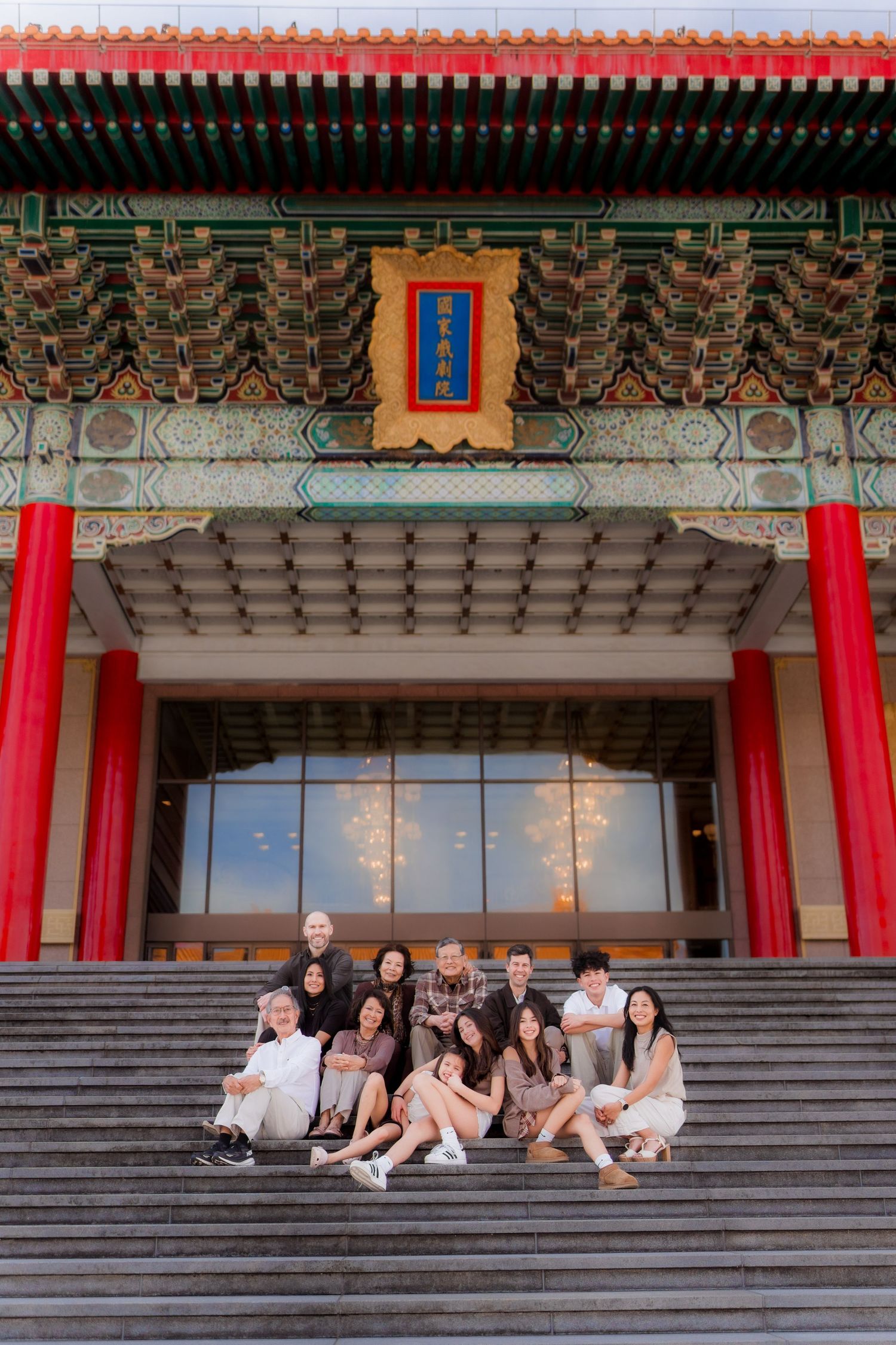 A group sits on the stone steps of a traditional Chinese temple with ornate architecture and red banners.
