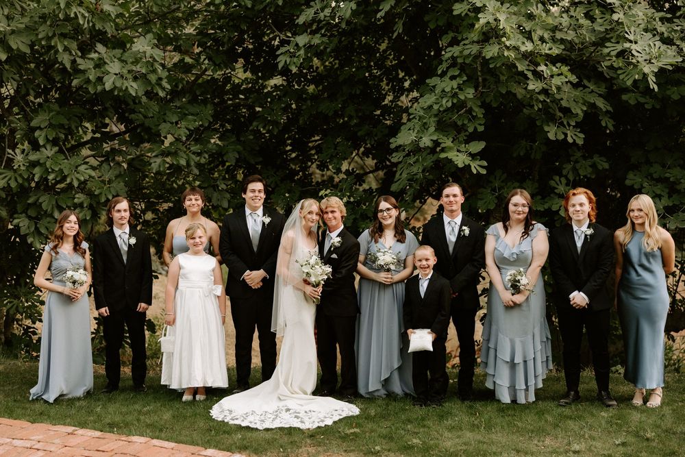 Wedding party members pose together outdoors in coordinated gray and white attire against a natural garden backdrop.