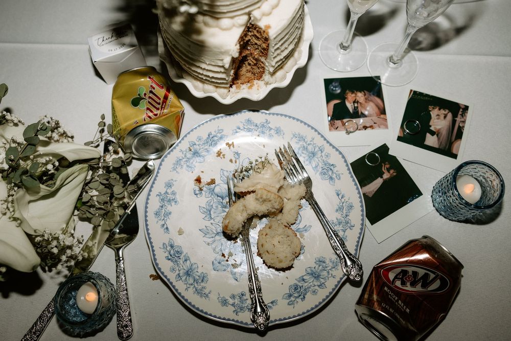 Overhead view of a vintage place setting with half-eaten pastry, photographs and decorative items on a patterned plate.
