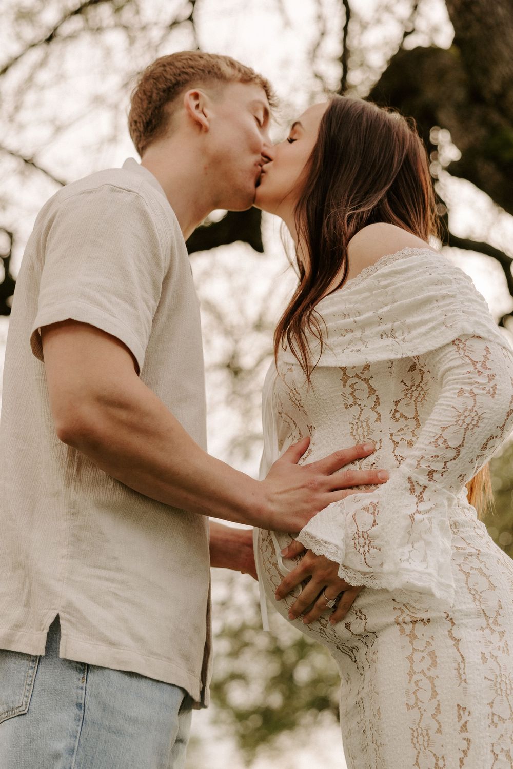 Romantic couple embracing in soft sunlight wearing white and casual attire.