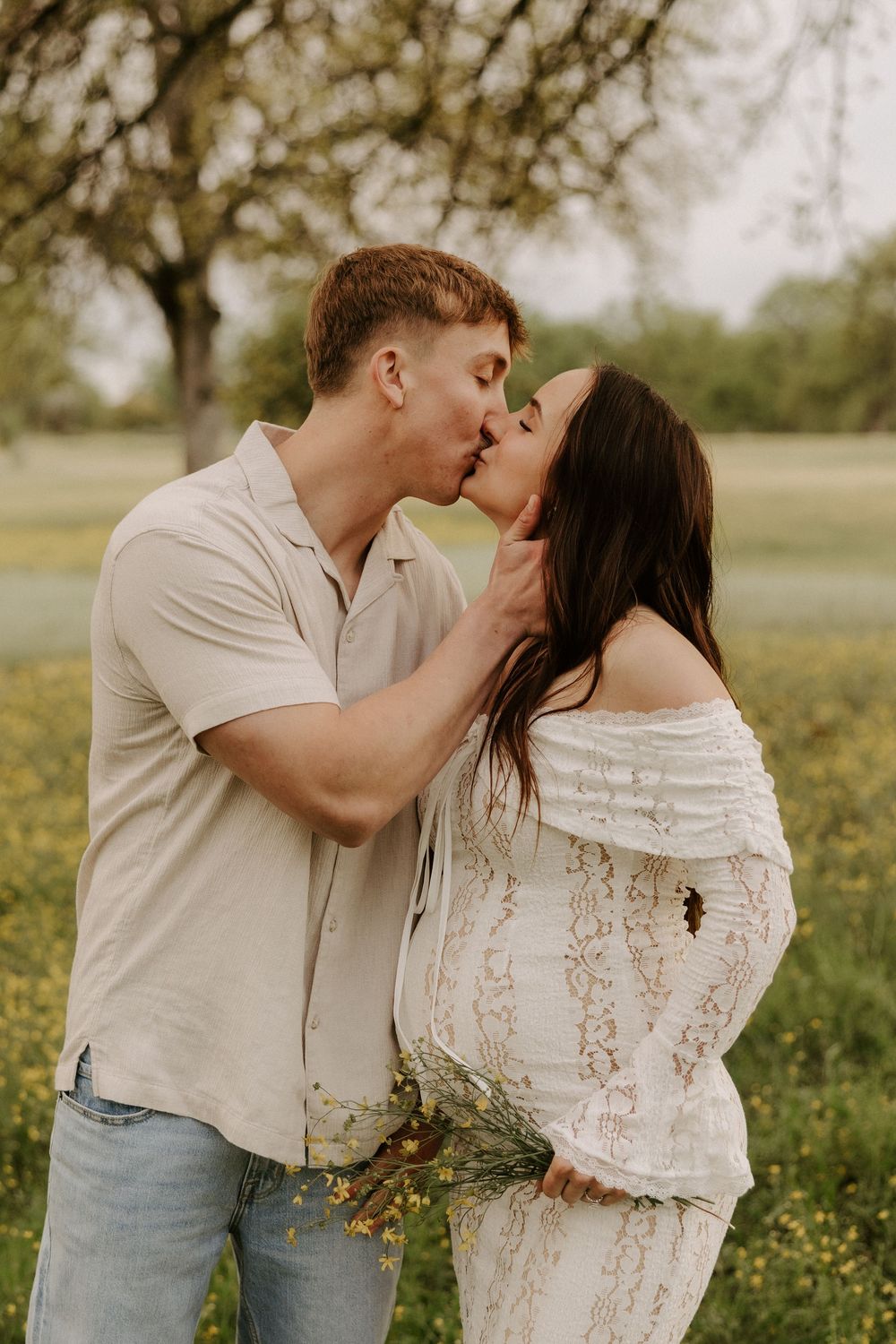 A couple shares romantic kisses in a spring meadow filled with yellow wildflowers while wearing casual attire.
