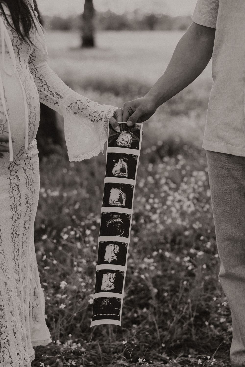 Black and white photo strip artfully displayed against a white lace dress in a meadow setting.