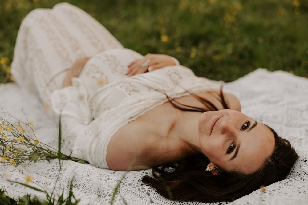 A figure in a white lace dress lies gracefully on grass during an outdoor photo session.