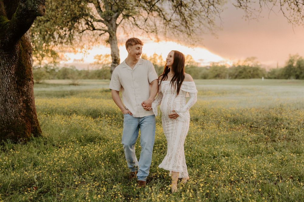 A couple stands together in a sunlit meadow during golden hour as the sun sets behind them creating a romantic atmosphere.