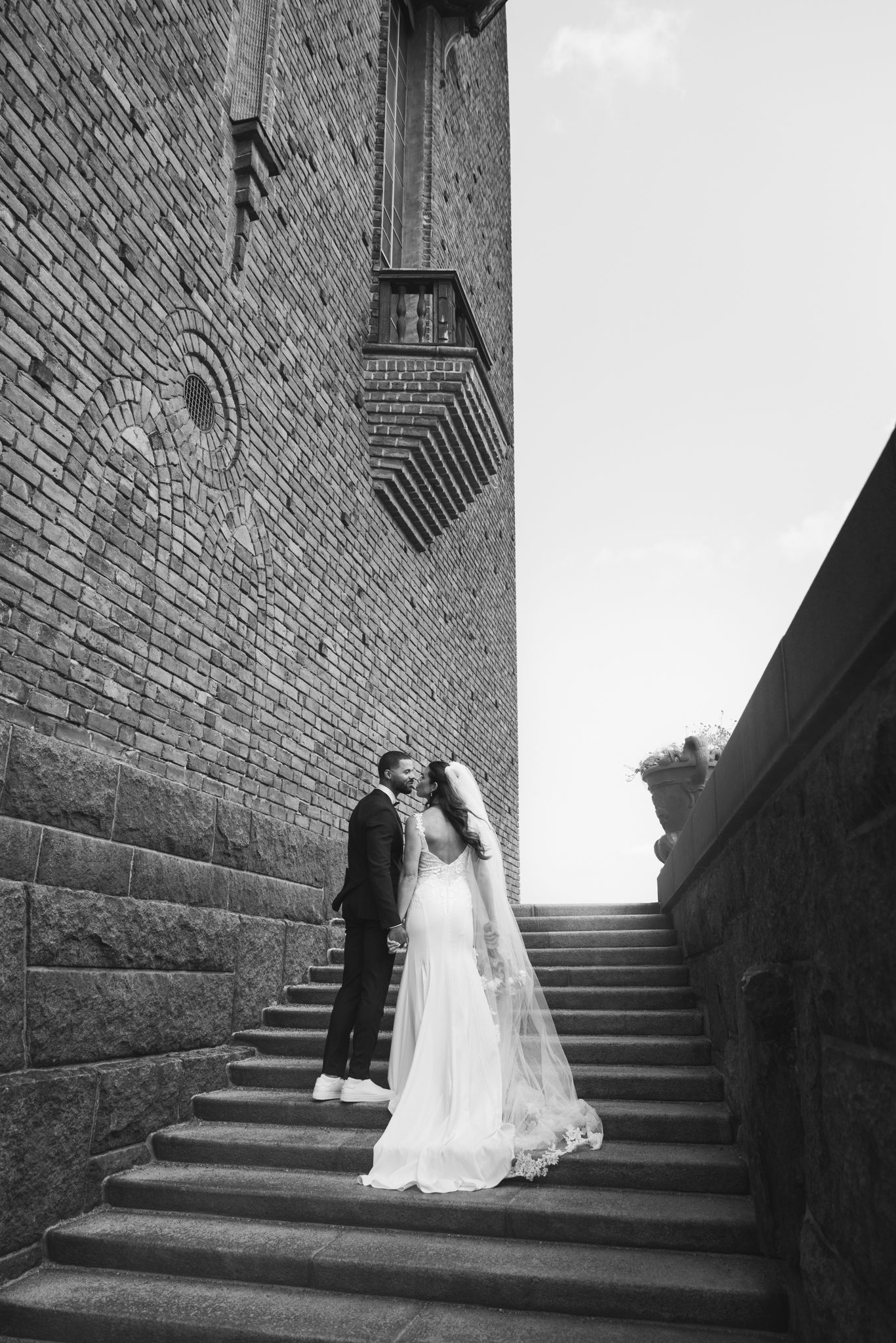 A couple shares an intimate moment on stone steps against a brick wall in black and white photography.