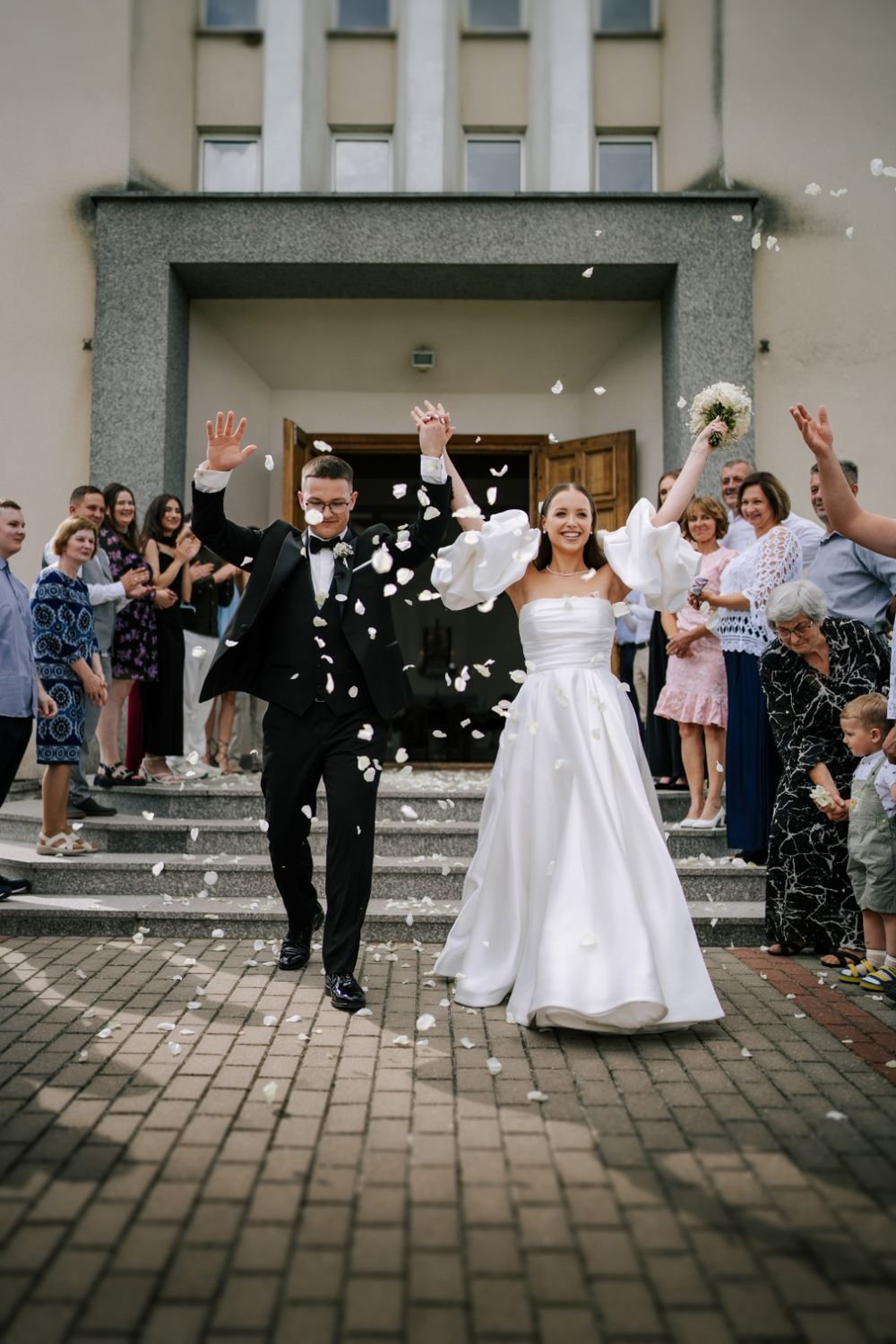 Newlyweds exiting church while guests throw confetti in celebration.