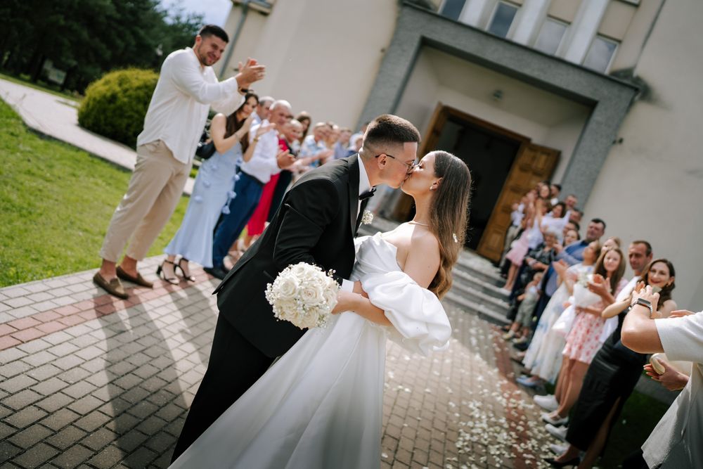 Wedding party celebrates outside a white church building on a sunny summer day.