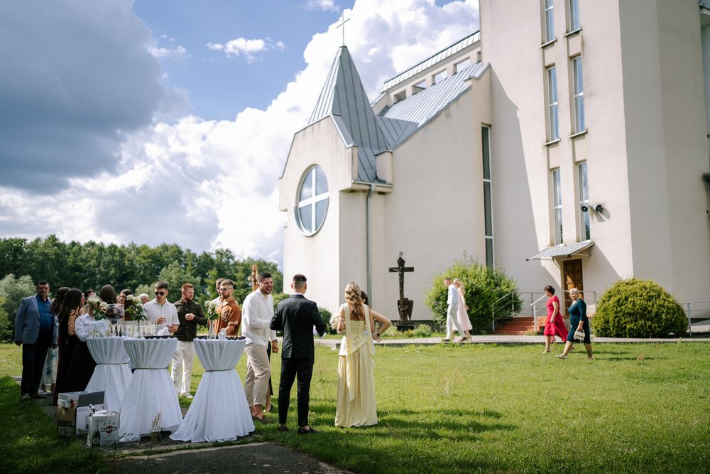 White church building with cross stands against blue cloudy sky during wedding ceremony.