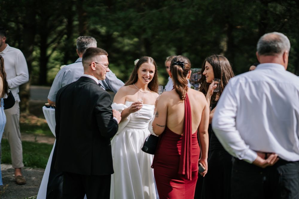 Wedding guests in formal attire gather outside during outdoor celebration.