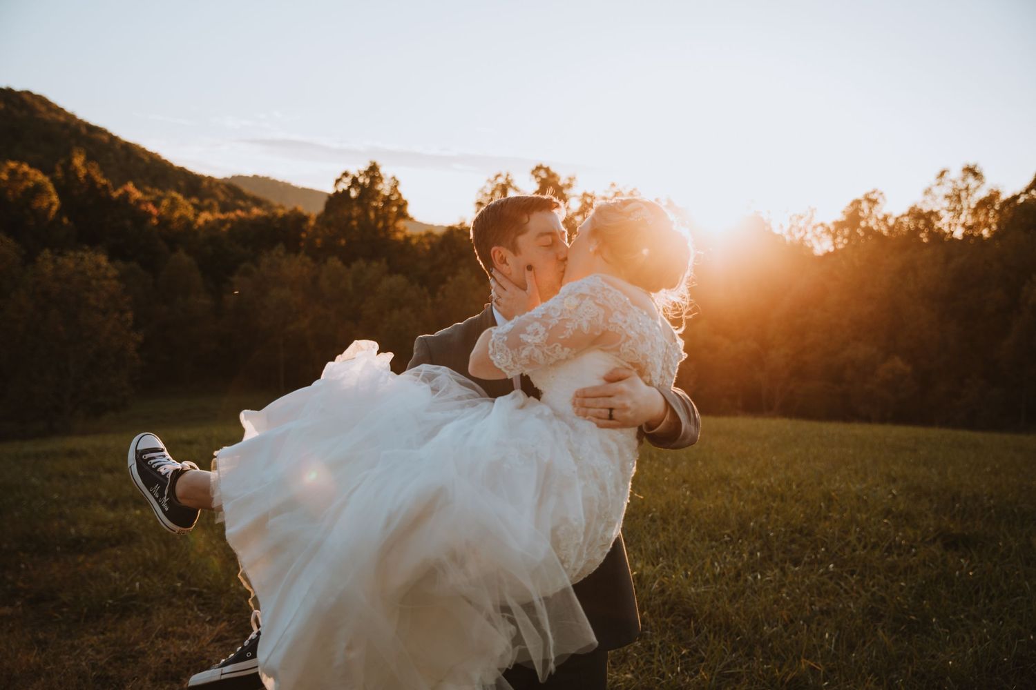 A groom lifts his bride in a sunlit mountain meadow during a golden hour wedding portrait.