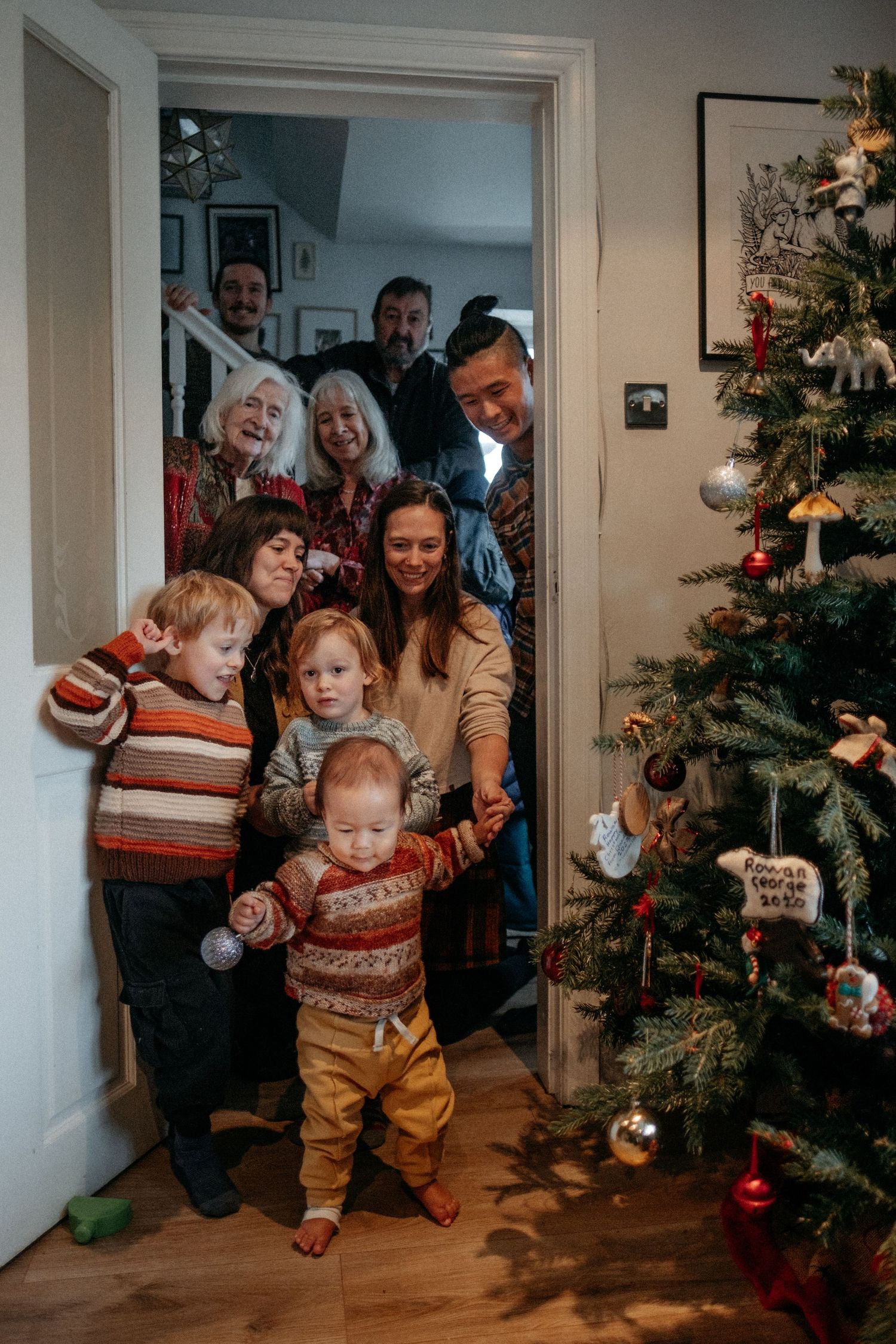 Family gathered in a doorway beside a decorated Christmas tree during a relaxed in-home lifestyle family photography session in Durham