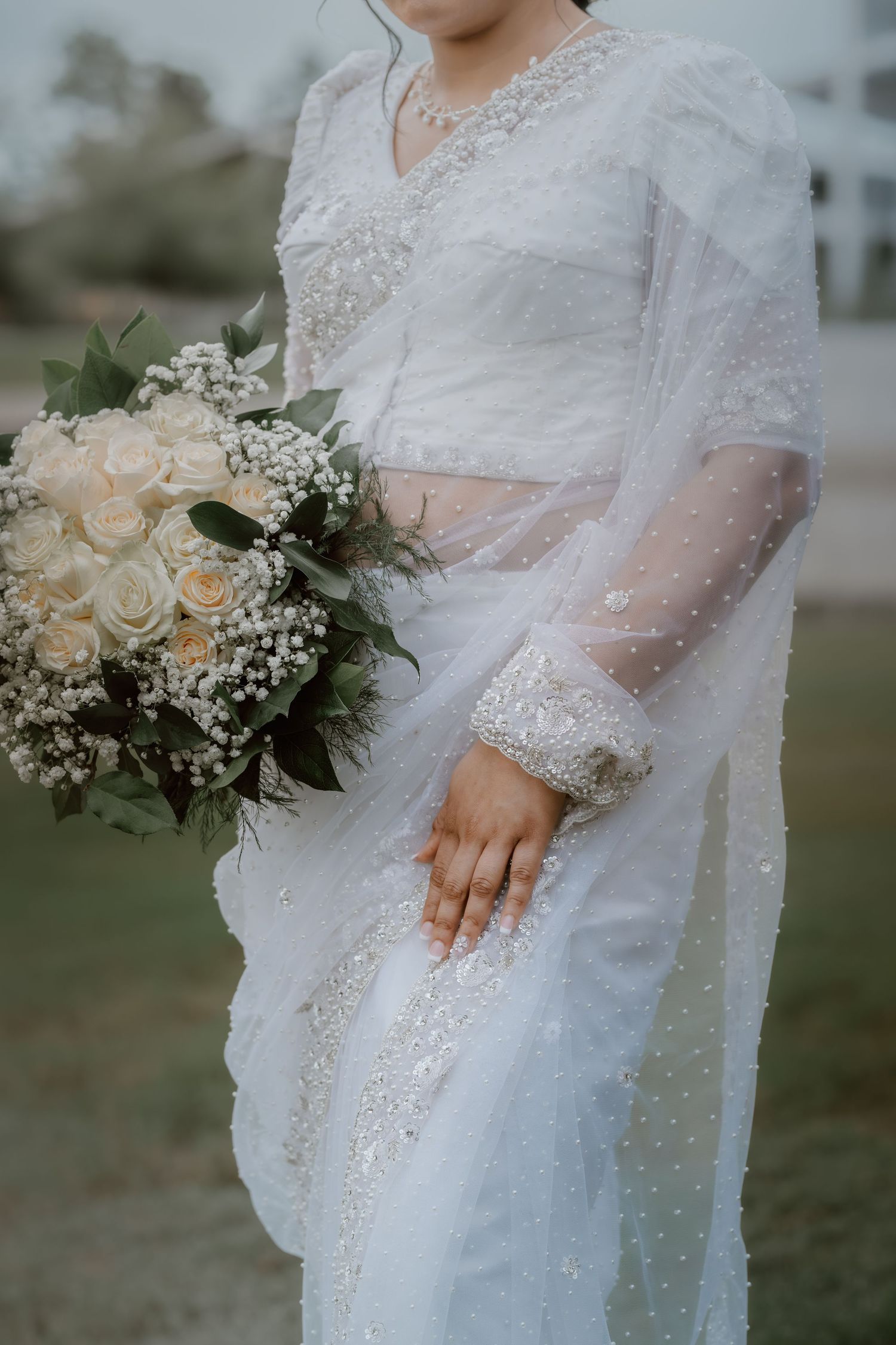 Close-up details of an elegant lace wedding dress with pearl embellishments and white rose bouquet.